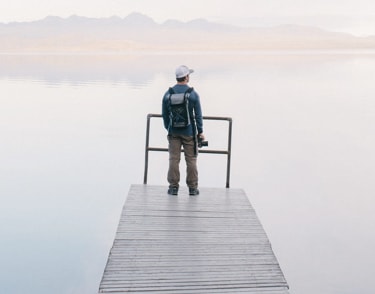  a man standing on a dock over water with a backpack and a camera