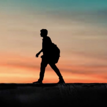 a silhouettte of a man walking across a field during sunset